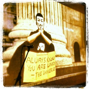still image from OCCUPY LOVE: Anonymous masked occupier with sign "Always remember you are loved - The Universe"